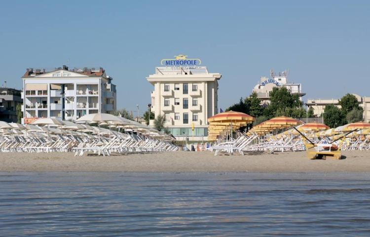 Spiaggia soleggiata con ombrelloni colorati, hotel Metropole sullo sfondo.
