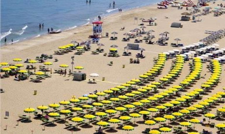 Spiaggia estiva affollata, ombrelloni gialli, mare blu, sole, gioia e relax.