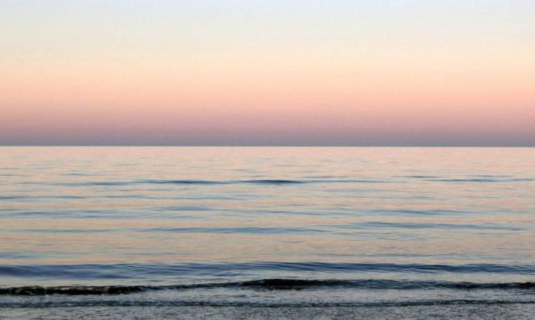 Tramonto sereno sul mare calmo, colori pastello sfumano dolcemente.