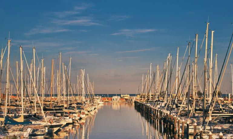 Barche a vela allineate, riflessi dorati sull'acqua al tramonto.